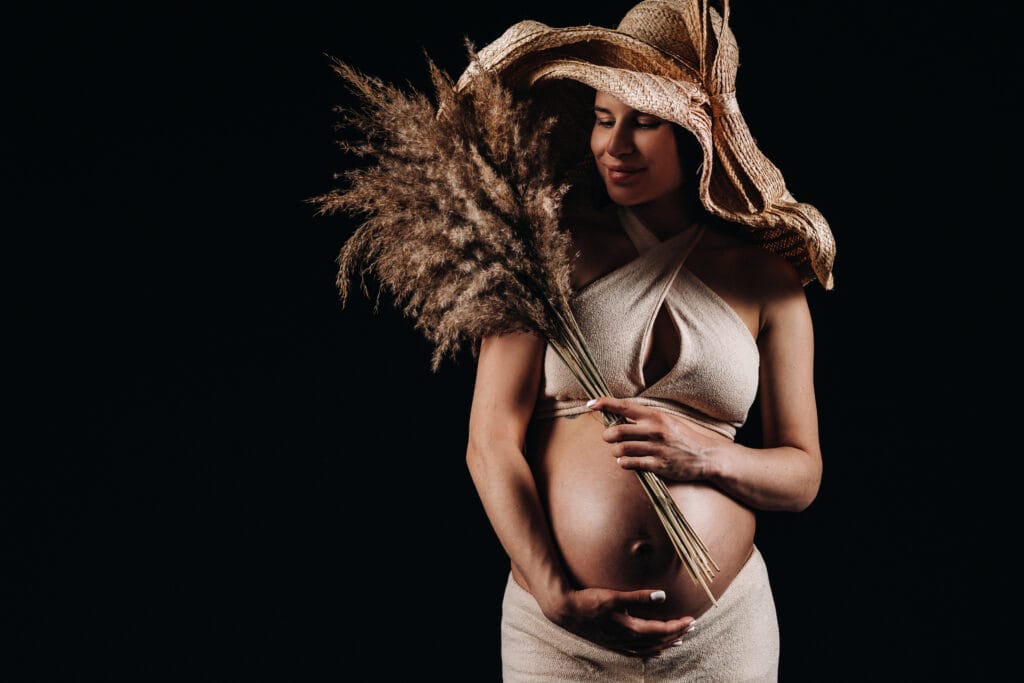 pregnant woman in a straw hat with beige clothes with a bouquet in her hands in the studio on a black background